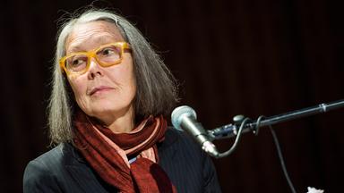 Porträtfoto einer älteren Frau mit schulterlangen grauen Haaren und einer Brille mit gelbem Kunststoffrahmen.