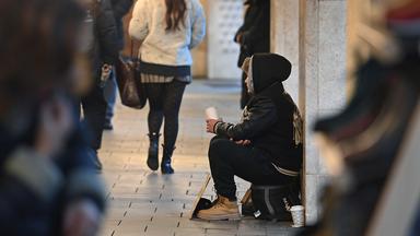 Ein junger Mann sitzt auf der Straße und bettelt.