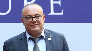 Porträtfoto von Atef Abu Saif, einem Mann im grauen Anzug mit kurzgeschorenen Haaren und Brille.