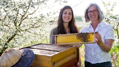 Zwei Frauen lächelnd vor einem Bienenstock