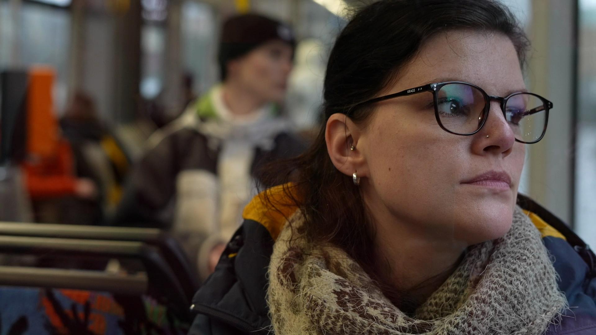 Claudia sitzt in der Tram schaut mit ernster Miene aus dem Fenster.