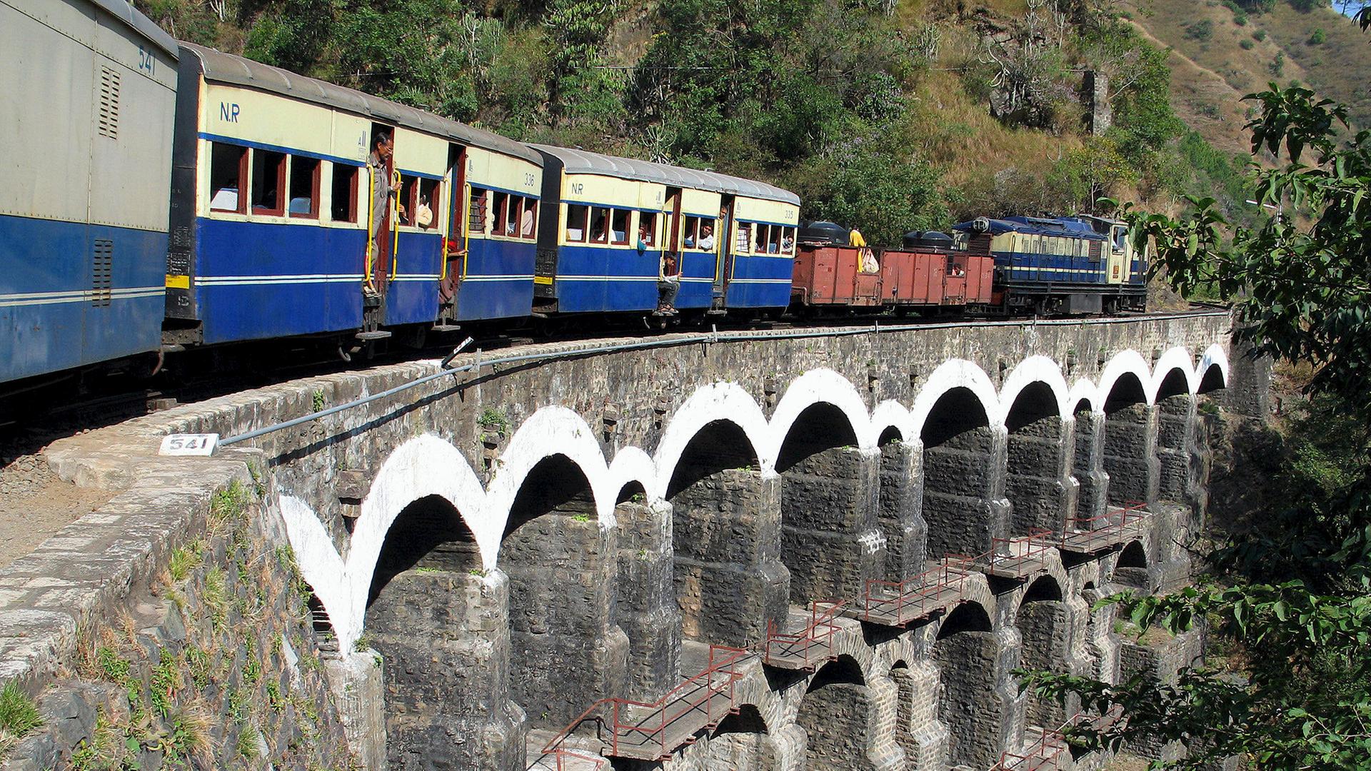 Ein blau-roter Zug der über eine Steinbrücke fährt.