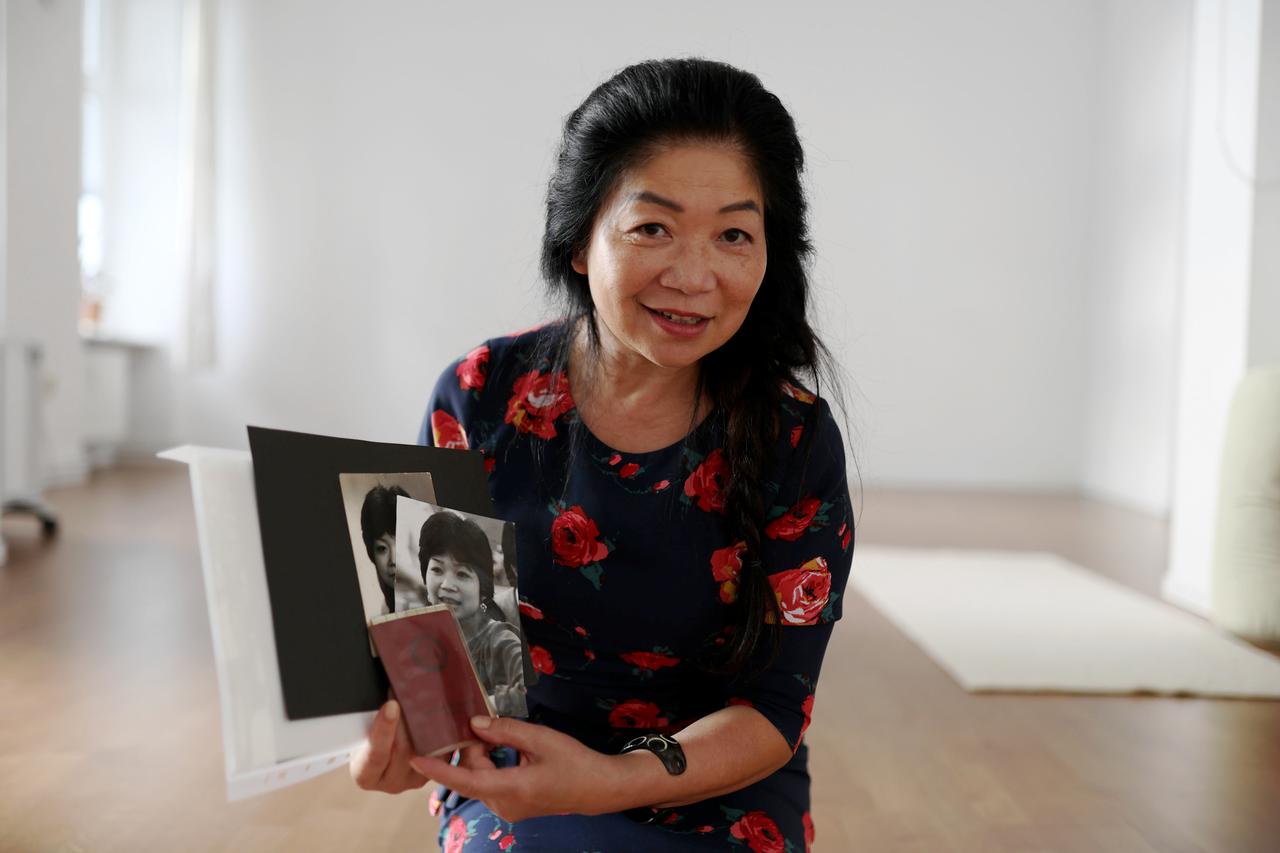 Frau mit vietnamesischem Aussehen hält einen Pass und Schwarzweiß-Fotos in der Hand, auf denen sie als junge Frau zu sehen ist.