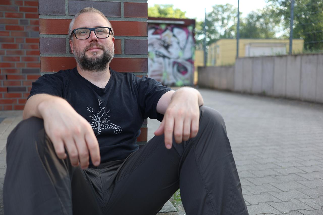 Mann mit Brille lehnt sitzend an einer Mauer