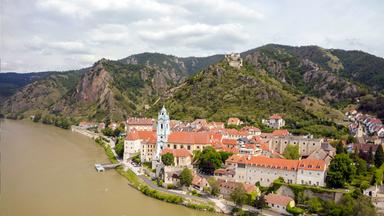 Blick auf Dürnstein in der Wachau mit der Donau im Vordergrund und den umliegenden Bergen im Hintergrund.