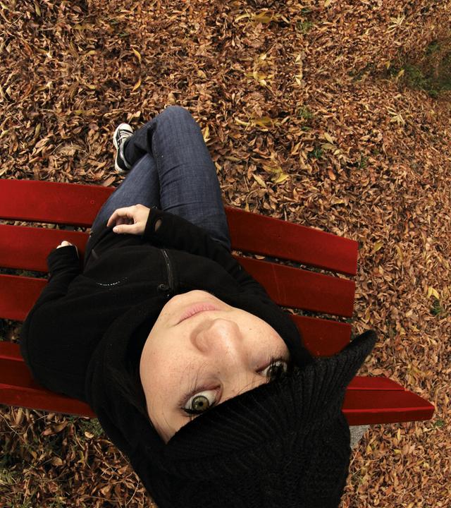 Junge Frau mit Kopfbedeckung sitzt auf Parkbank