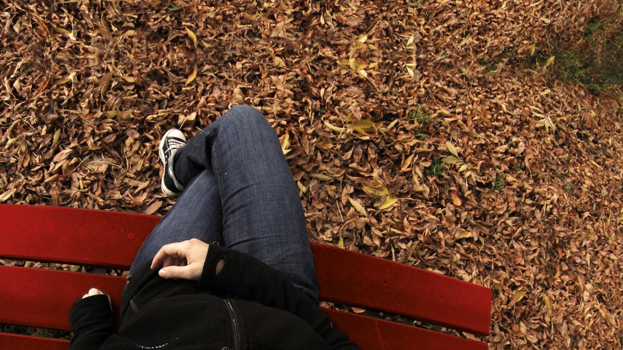 Junge Frau mit Kopfbedeckung sitzt auf Parkbank