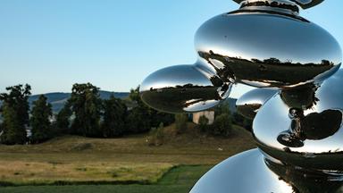 In einer grünen Landschaft steht eine Skulptur aus silbrig glänzenden Blasen.