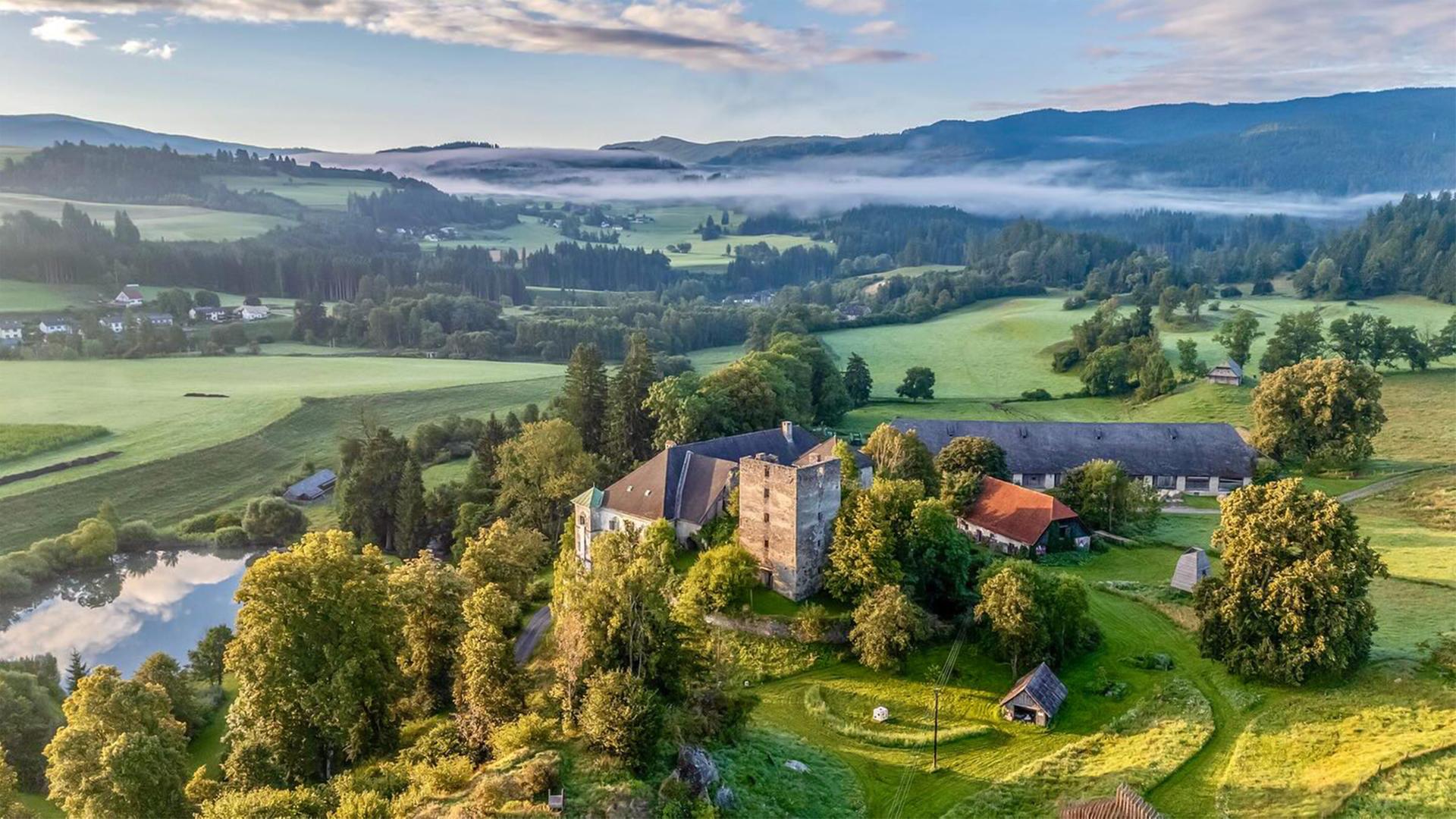 Ein historisches Schloss liegt eingebettet in eine hügelige Landschaft.
