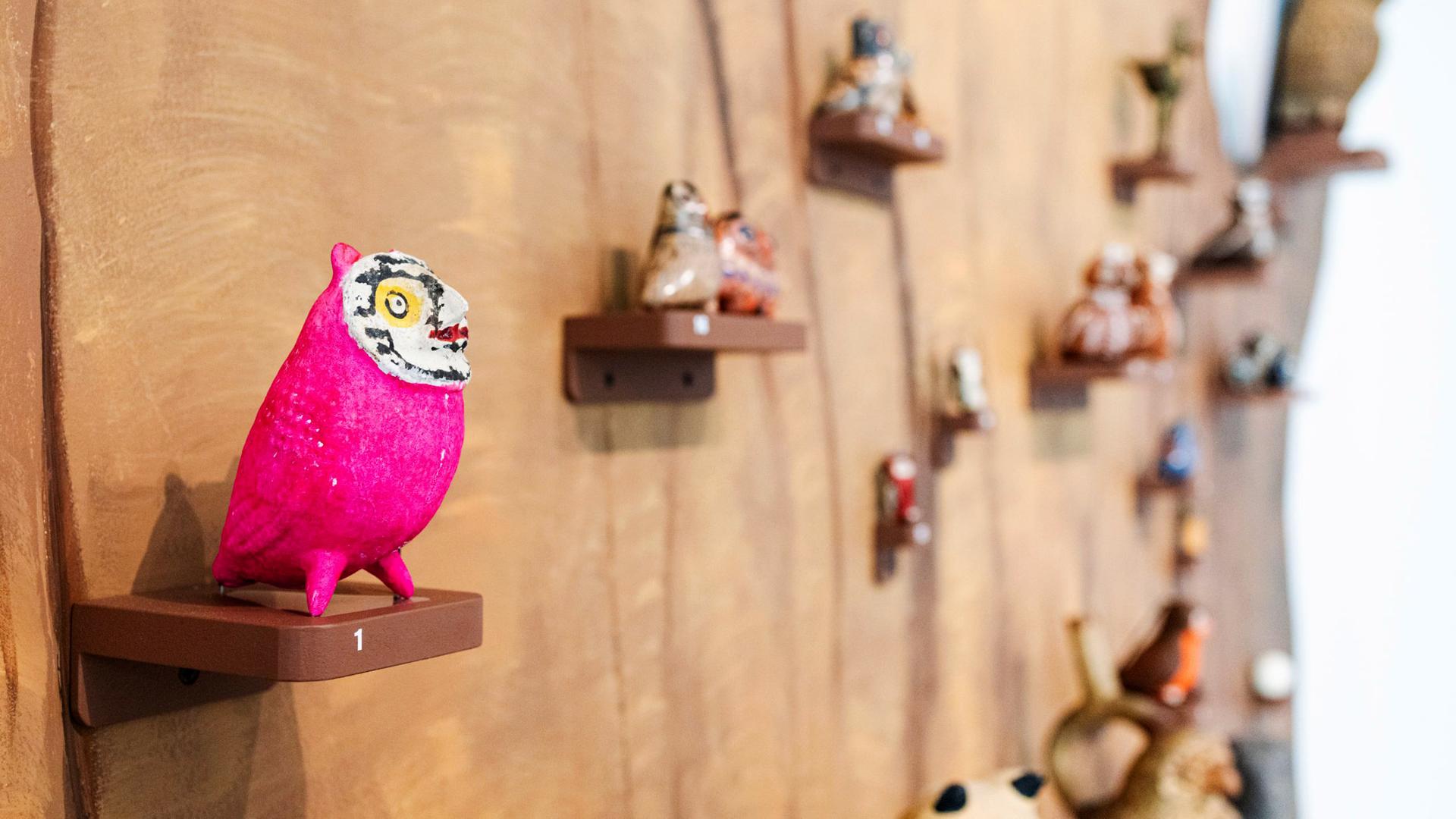 Man sieht verschiedene Eulen aus Ton an einer Wand ausgestellt.