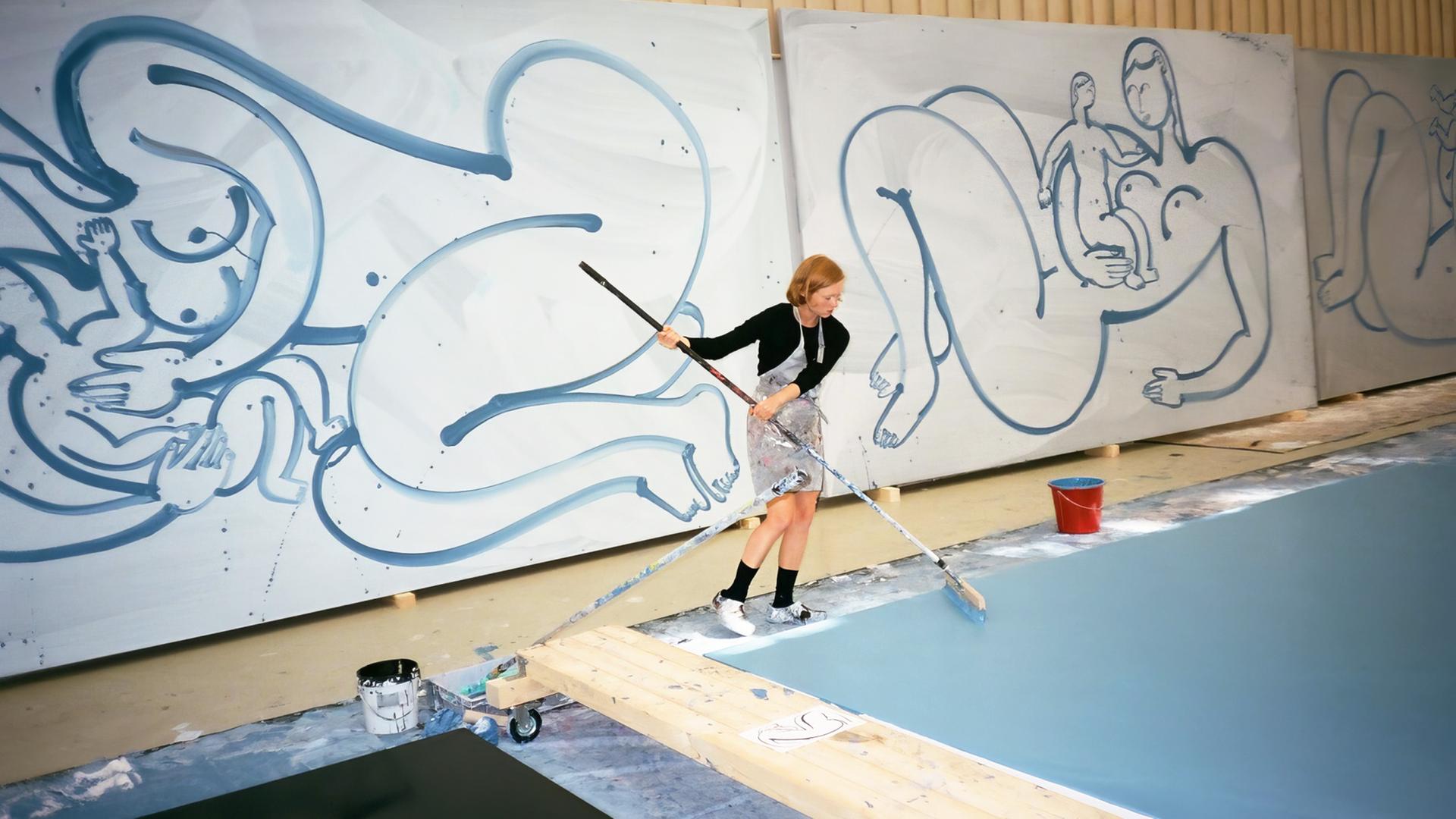 Man sieht eine Künstlerin im Atelier großformatige Biloder malen.
