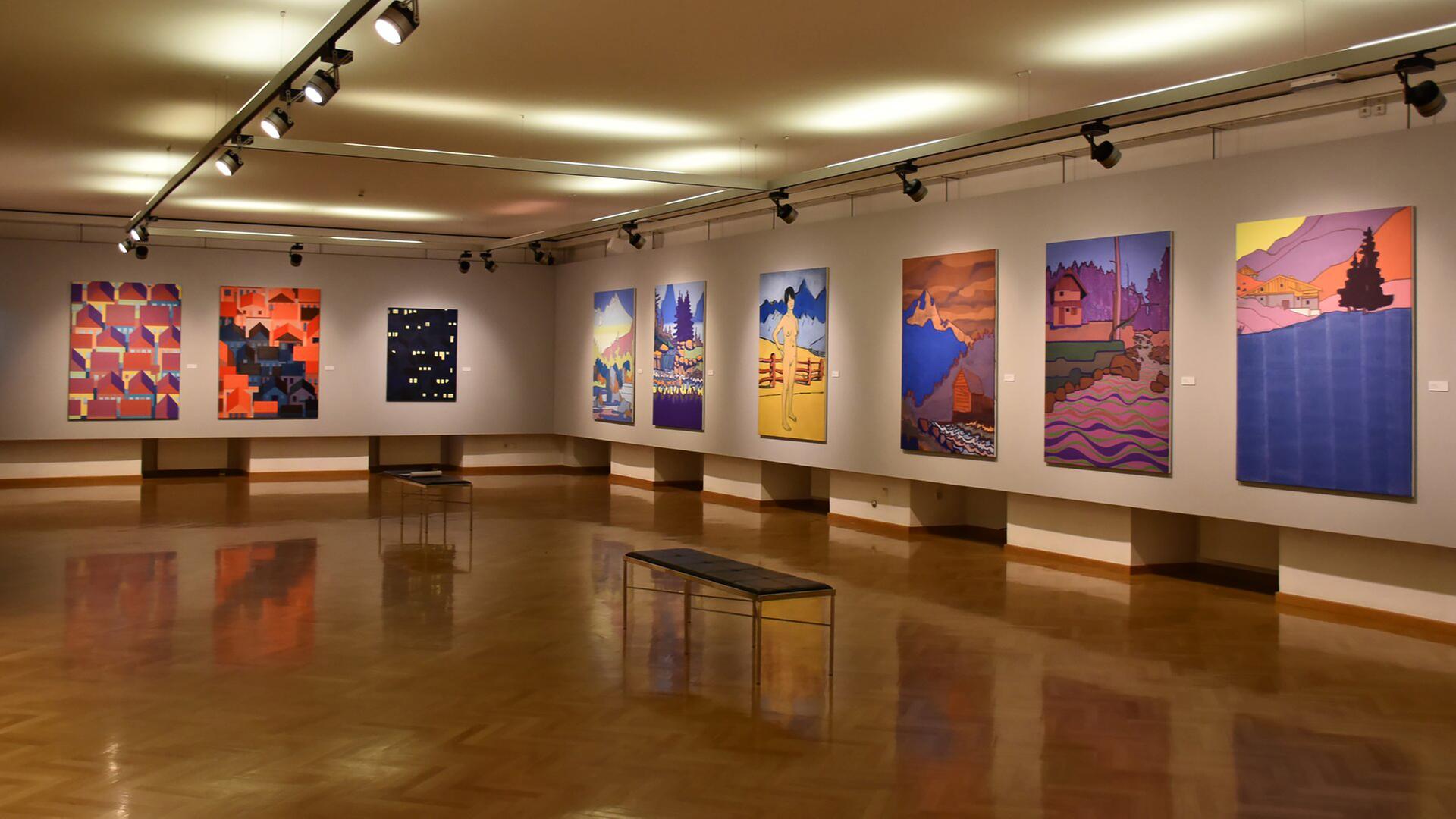 In einem Ausstellungsraum sieht man moderne, bunte Gemälde an den Wänden.
