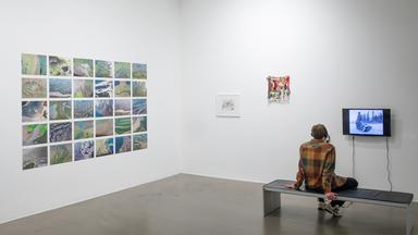 In einem Ausstellungsraum sitzt ein Mann der sich die Exponate ansieht. 