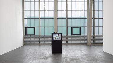 In einem Ausstellungsraum mit großen Fenstern steht eine Videoinstallation.