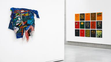 In einem Ausstellungsraum sieht man bunte Kunstwerke an den Wänden.
