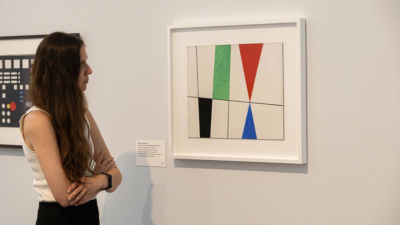 In einem Ausstellungsraum schaut eine Frau ein modernes Gemälde an.