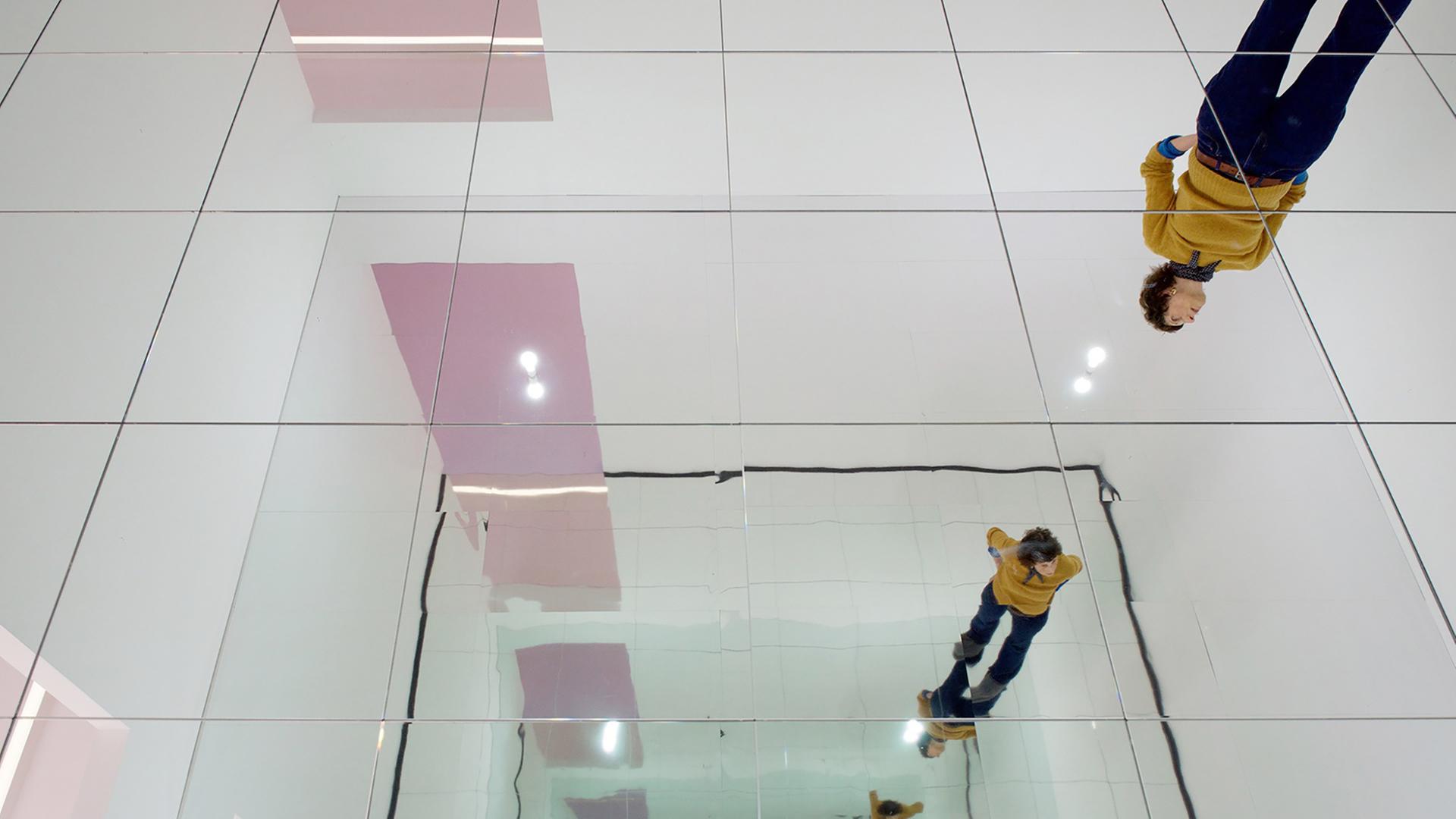 In einem Ausstellungsraum spiegelt sich eine Frau in einer Spiegel-Installation, die eine unendliche Reihe Spiegelbilder erzeugt.