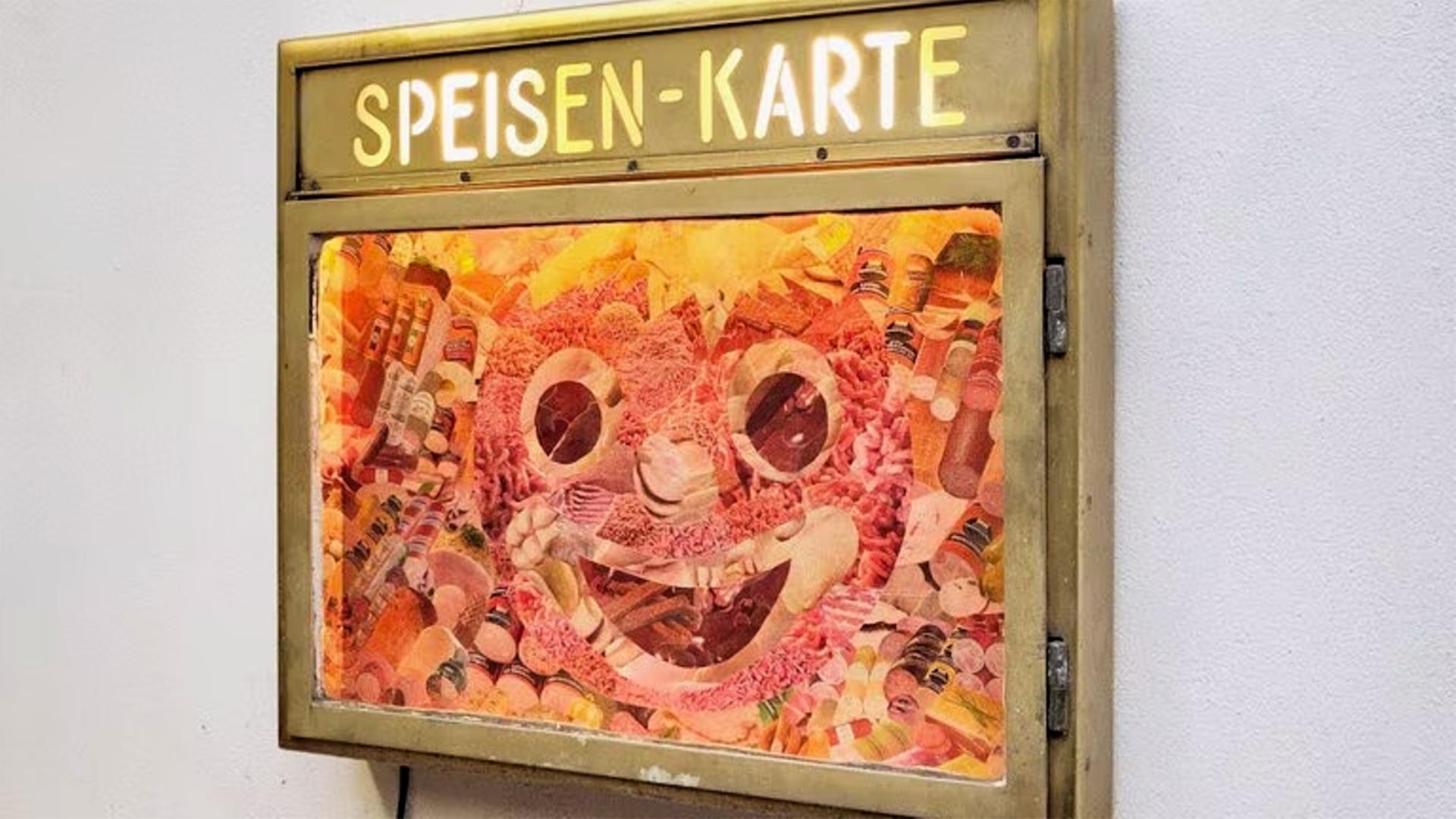Man sieht einen Restaurant-Schaukasten der eine Collage in Form einer Gesichtswurst enthält.