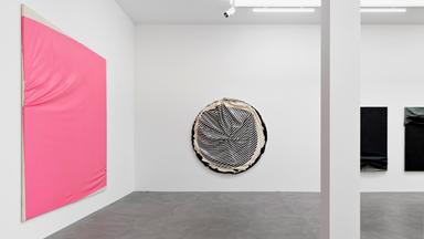 In einem Ausstellungsraum hängen pinkfarbene und schwarz-weiße Objekte an den Wänden.