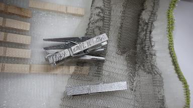 Auf einem feingetrickten Gewebe liegen silber-farbene Wäscheklammern.