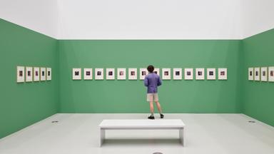 In eienm Ausstellungsraum schaut ein Mann sich Fotografien an, die an einer grünen Wand hängen.