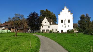 Man sieht ein historisches Gebäude in grüner Landschaft.