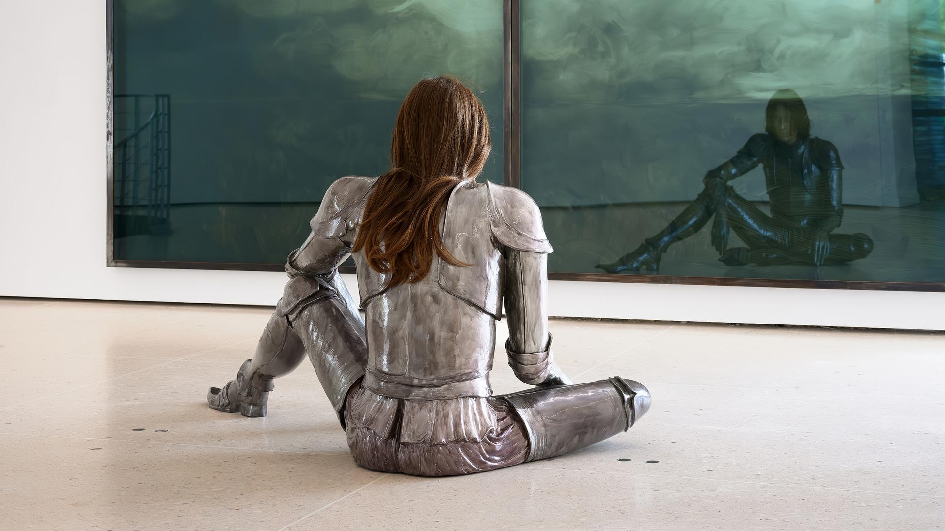 Eine Frau in Rüstung sitzt vor einem Kunstwerk.