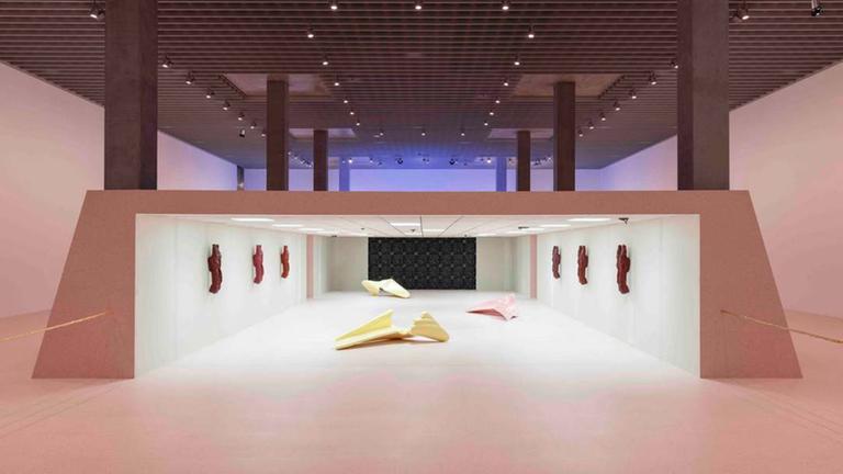 In einer großen Halle ist ein Raum installiert, in dem verschiedene Skulpturen zu sehen sind.