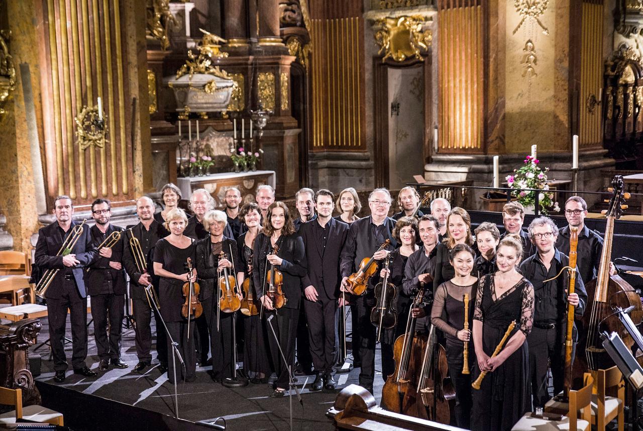 Musiker und Musikerinnen - teilweise mit ihren Instrumenten - stehen vor einem Barockaltar.