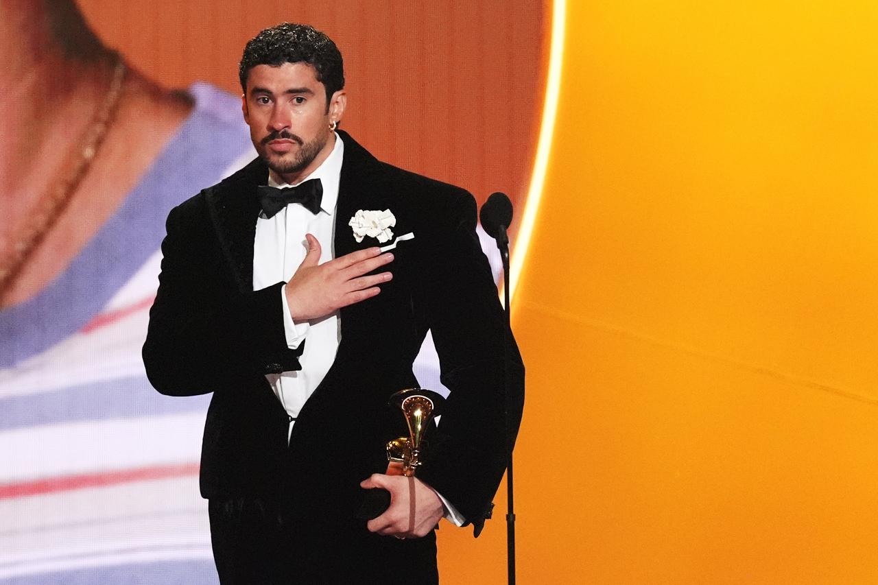 Ein dunkelhaariger Bann mit Bart trägt einen Smoking und steht auf einer Bühne. In der linken Hand hält er ein goldenes Grammophon, während er sich die rechte aufs Herz legt.