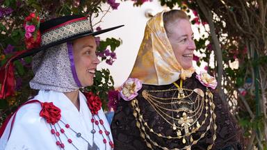 Zwei Frauen und ein Mann in aufwendiger traditioneller Kleidung der Gruppe Es Xacoters stehen lachend beisammen vor einer blühenden Bougainvillea auf Formentera.
