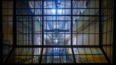 Blick durch ein Gitter in einen Gefängnisinnenhof.