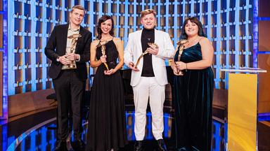 Zwei Frauen und zwei Männer in Abendgarderobe stehen auf einer Bühne und halten Preise in den Händen.