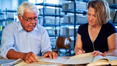 Prof. Michael von Cranach und Archivarin Petra Schweizer-Martinschek sitzen am Schreibtisch vor Akten.
