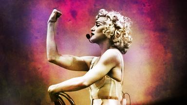 rägt ein Headset-Mikrofon und hebt in einer kraftvollen Geste ihren rechten Arm, um ihren angespannten Bizeps zu zeigen. Die Aufnahme ist in Schwarz-Weiß gehalten und betont ihre Entschlossenheit und Präsenz. 