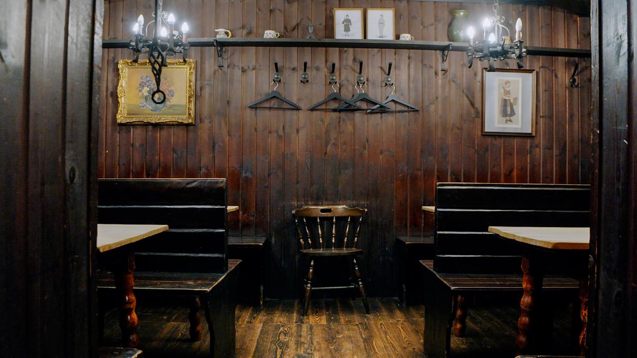 Dunkle Holzbänke, ein Stuhl und Tische vor einer dunklen Holzwand