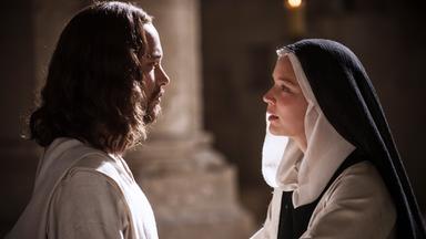 Jesus (Jonathan Couzinié) blickt Benedetta (Virginie Efira) aufmerksam an, während die Nonne ihn mit beiden Händen an den Armen anfasst.