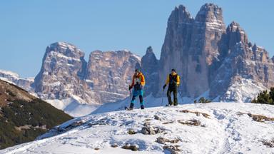 Zwei Personen auf Schneeschuhen, im Hintergrund die Drei Zinnen.