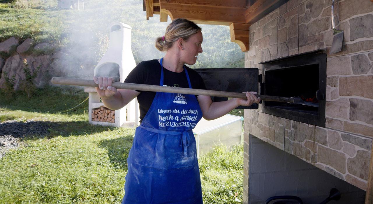 Eine Frau steht vor einem Steinofen mit blauer Schürze