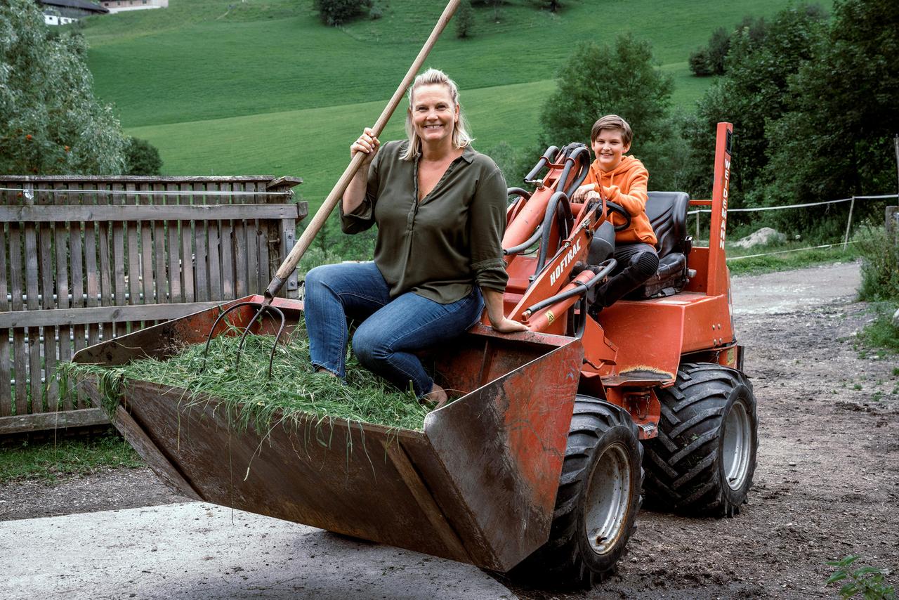 Frau in Traktorschaufel, Traktor wird von Jungen gefahren