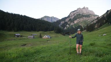Eine Frau steht auf der Weide vor einer Alp.