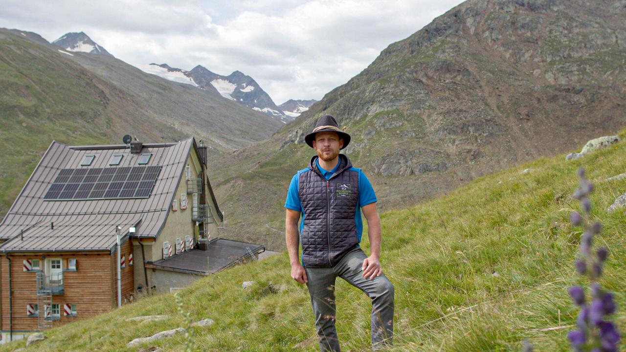 Junger Mann, der vor einer Berghütte für ein Foto posiert
