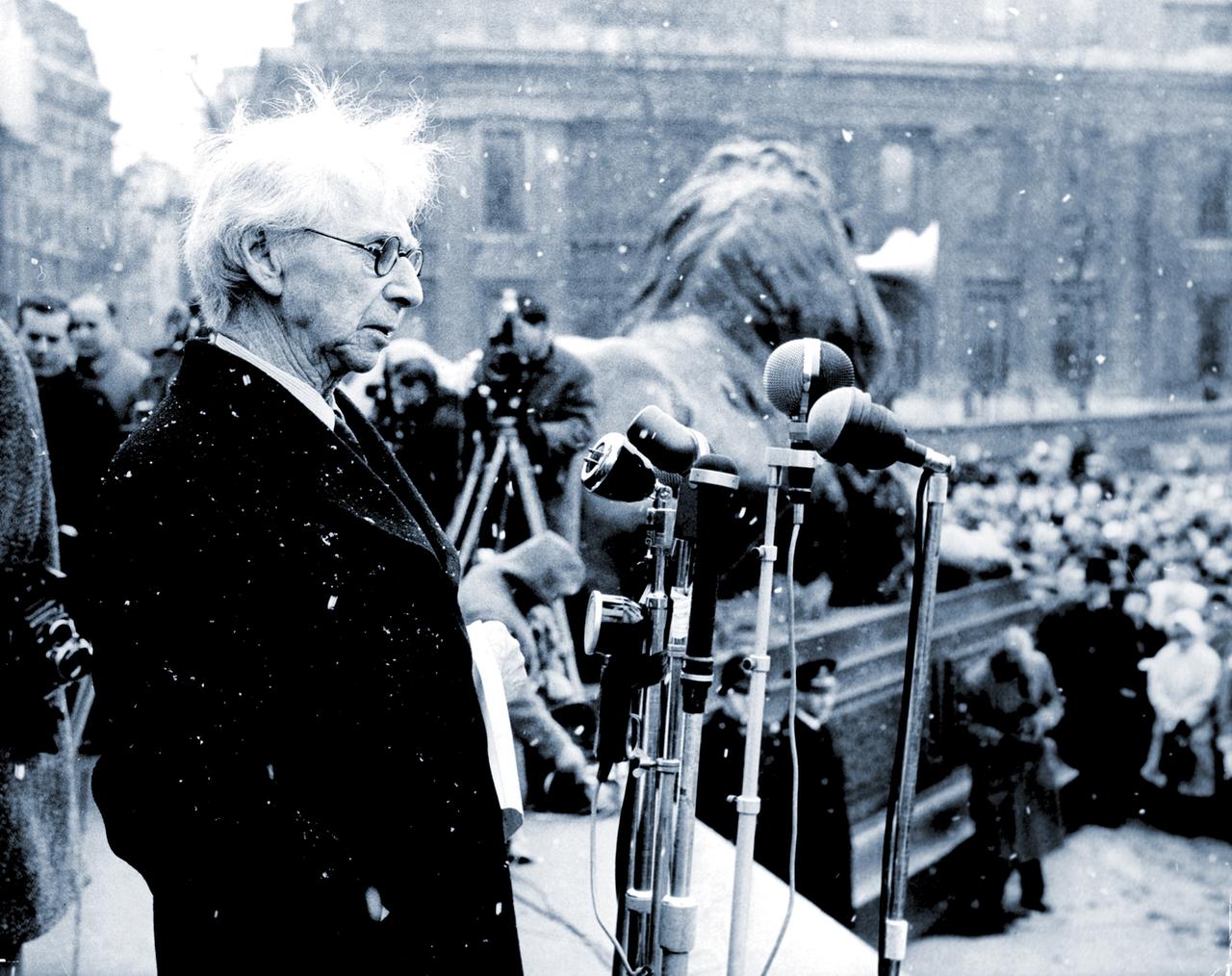 Philosoph Bertrand Russell steht auf einer Bühne am Trafalgar Square in London und spricht in mehrere Mikrofone.