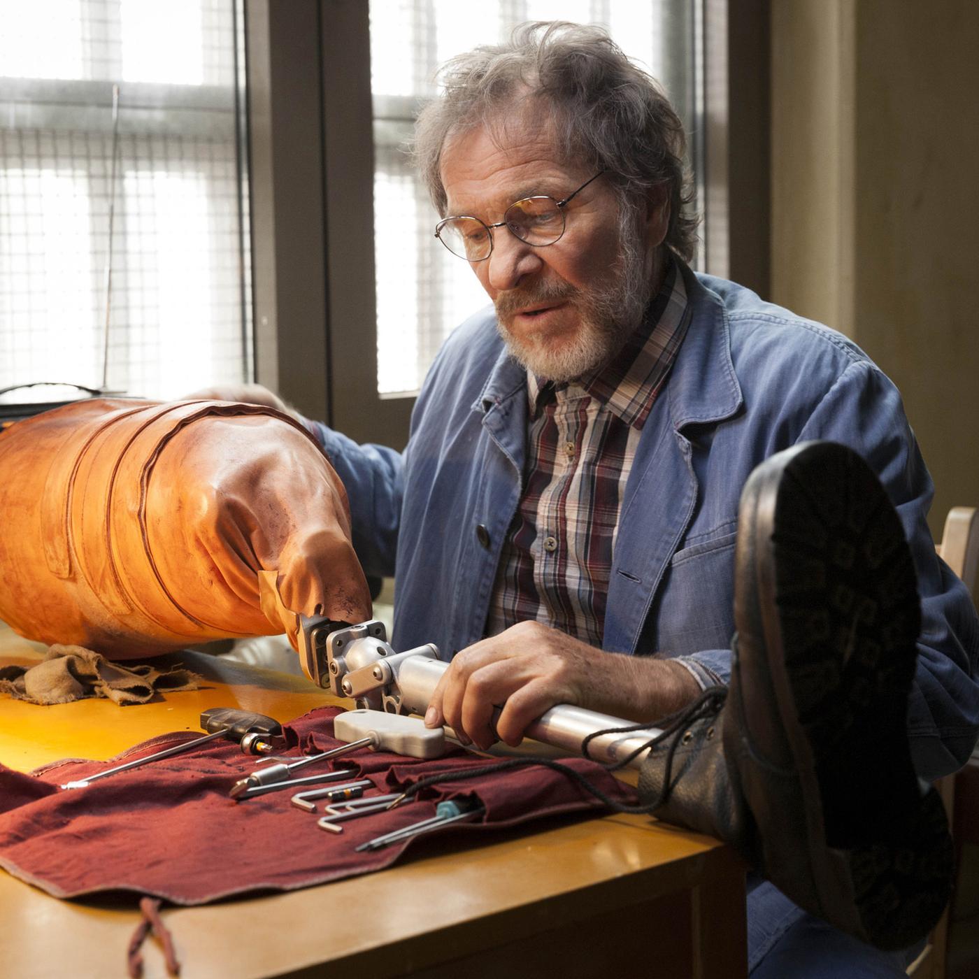 Joseph Komalschek (Götz George) sitzt am Tisch und arbeitet an einer Beinprothese.