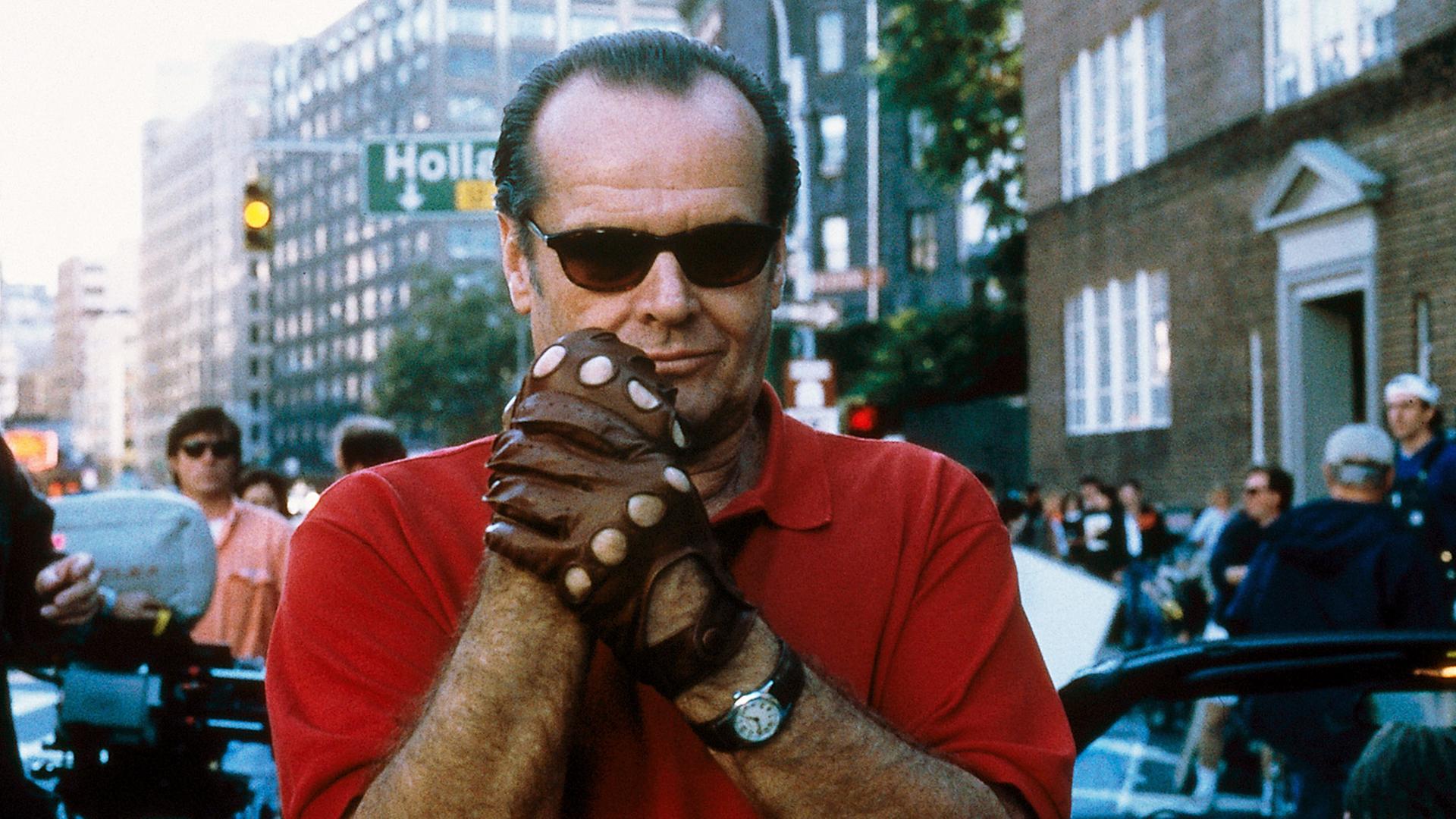 Ein Mann mit schwarzer Sonnenbrille und rotem Pulli reibt sich die Hände, die in braunen Lederhandschuhen stecken