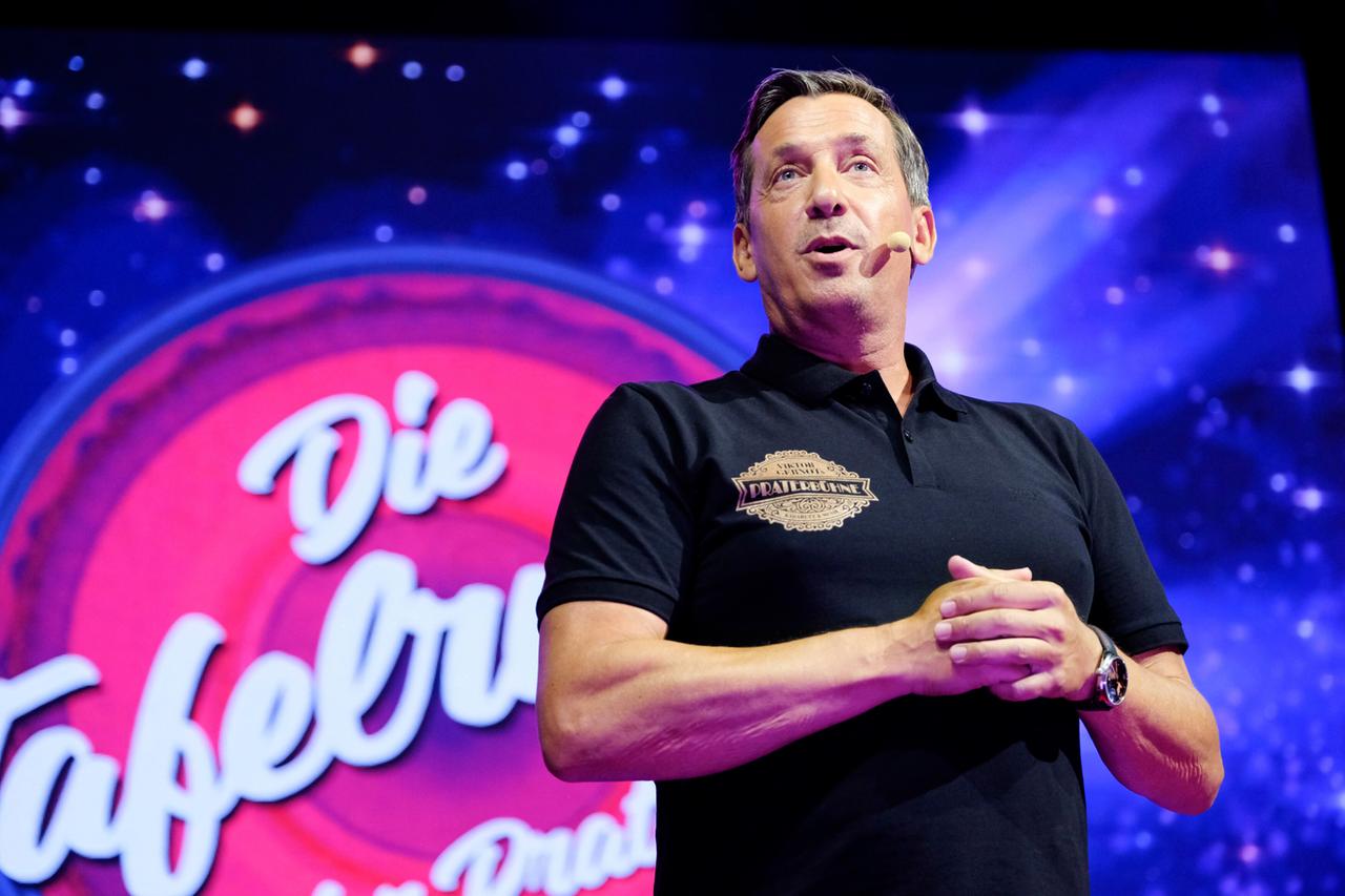 Ein Mann in einem dunklen Poloshirt mit einem Headset steht auf einer blau angestrahlten Bühne