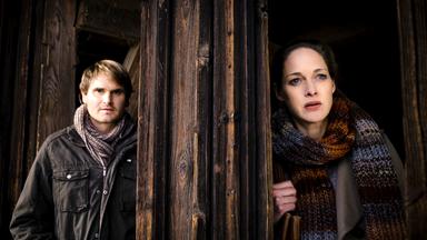 Tom (Fabian Hinrichs) und Anna (Sophie von Kessel) stehen vor einem Holzeingang und beobachten eine Situation.