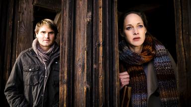 Tom (Fabian Hinrichs) und Anna (Sophie von Kessel) stehen vor einem Holzeingang und beobachten eine Situation.