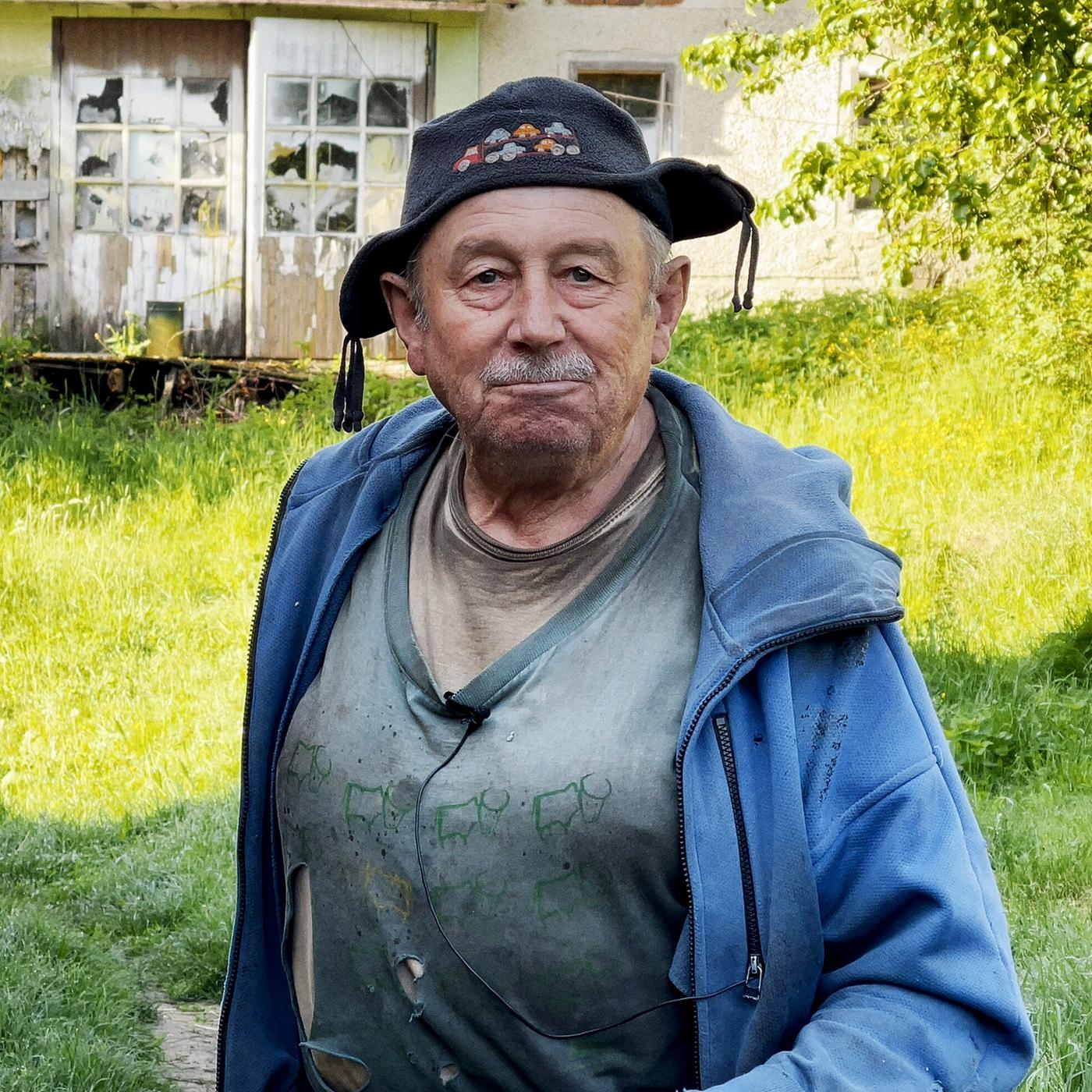 Ein Mann mit einer Kappe und blauer Jacke steht auf einer grünen Wiese