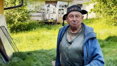 Ein Mann mit einer Kappe und blauer Jacke steht auf einer grünen Wiese